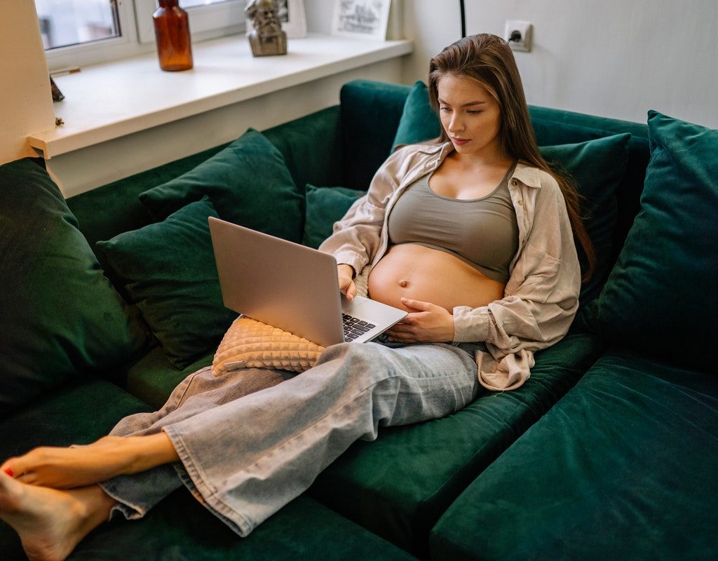 Pregnant woman relaxing on a couch with her laptop