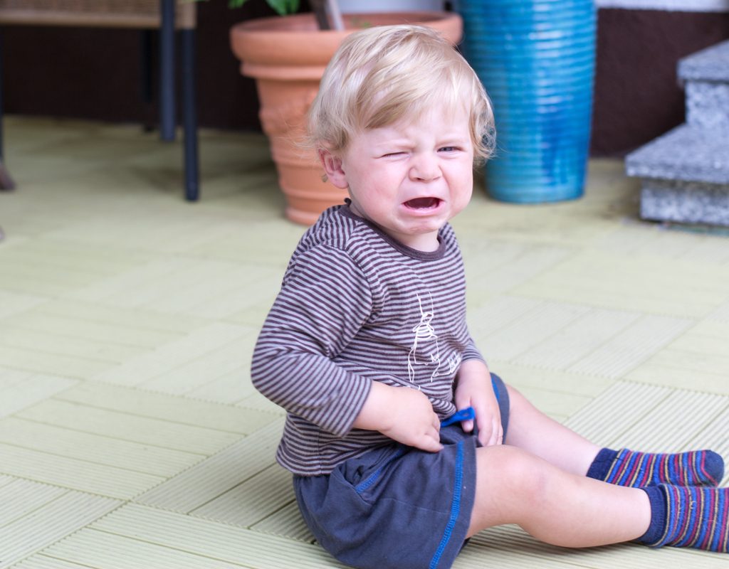 A toddler boy sitting down throwing a tantrum.