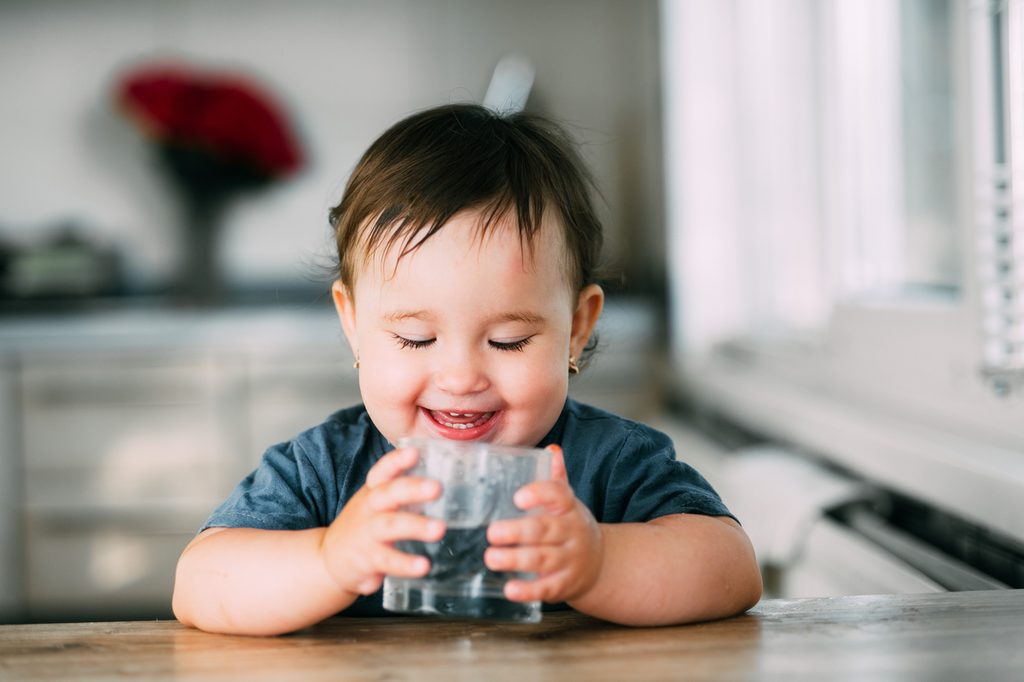 A toddler holding a glass of water.
