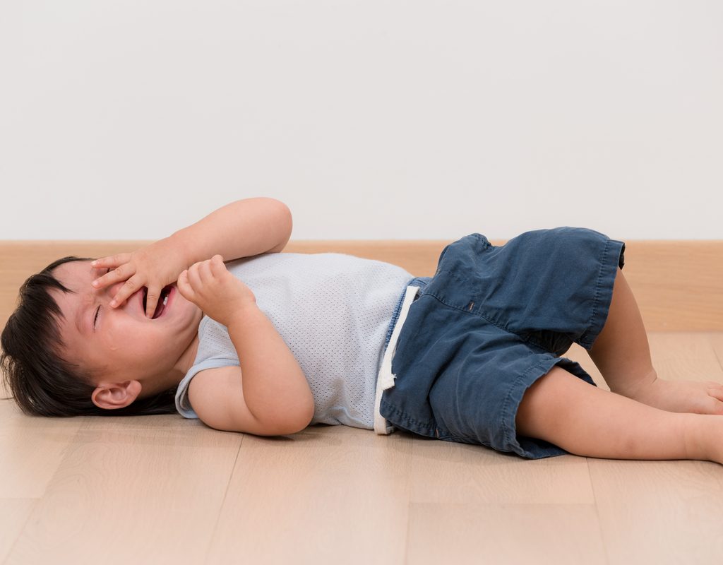 A toddler boy throwing a tantrum on the floor.