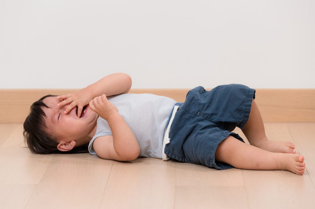 A toddler boy throwing a tantrum on the floor.