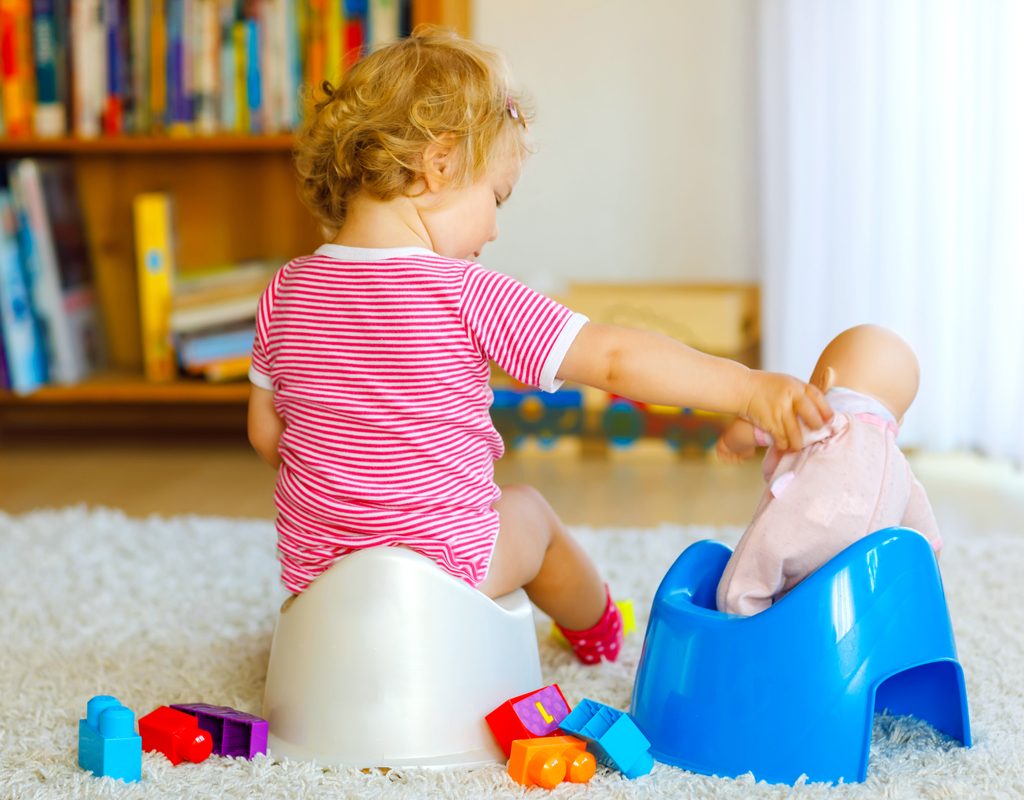 A little girl on a potty holding a doll on another potty.