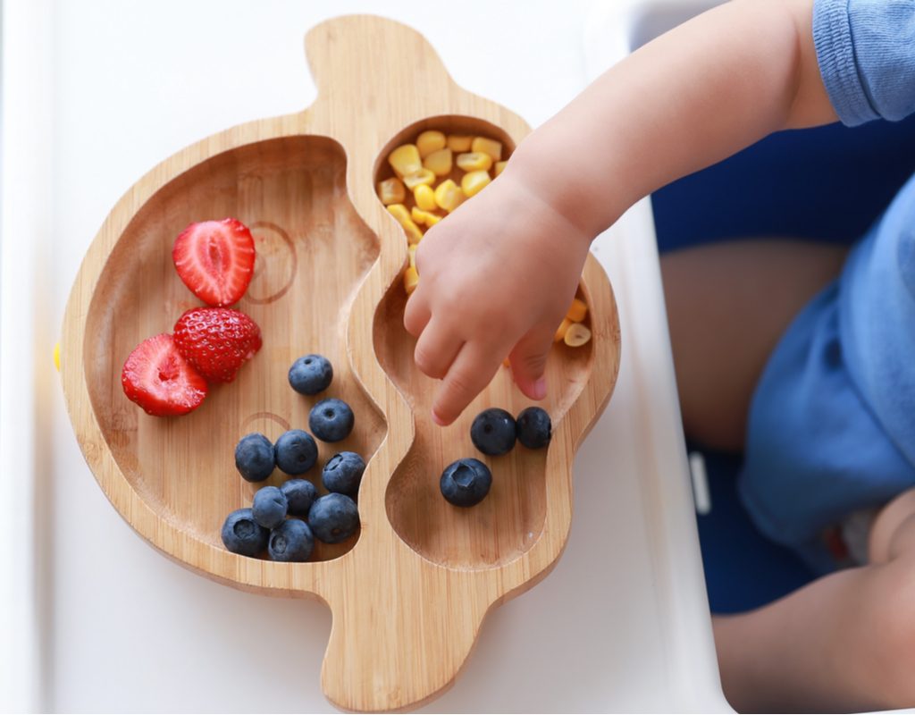 A toddler grabbing some food off of a plate.