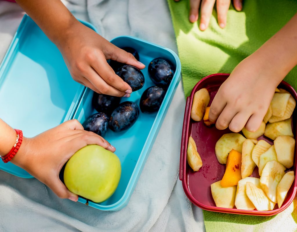 Kids grabbing fruit pieces out of lunchboxes.