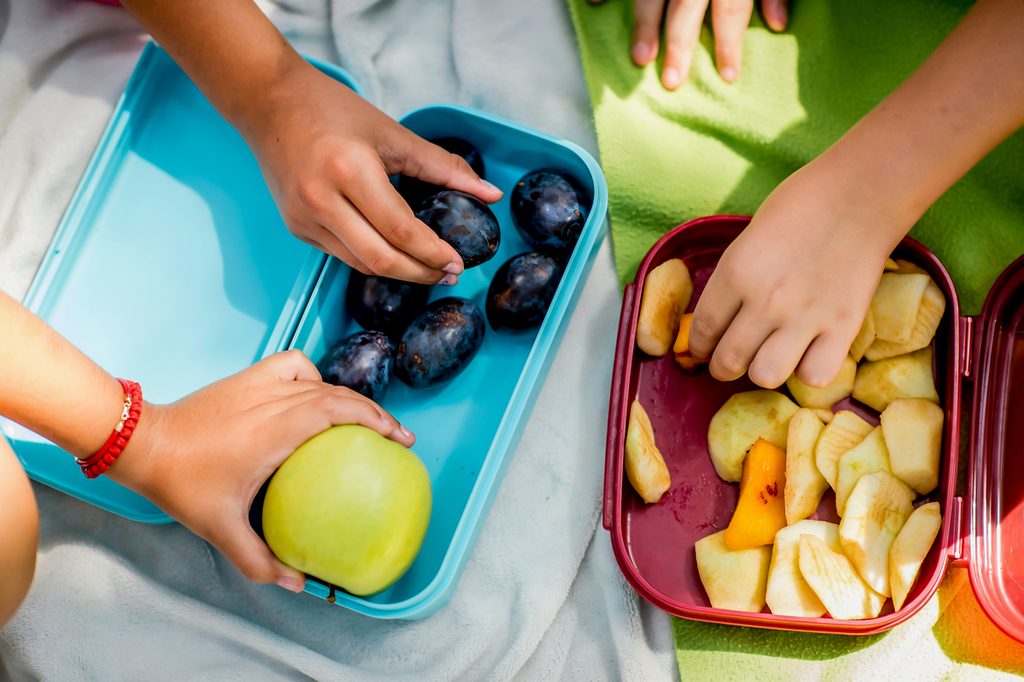 Kids grabbing fruit pieces out of lunchboxes.