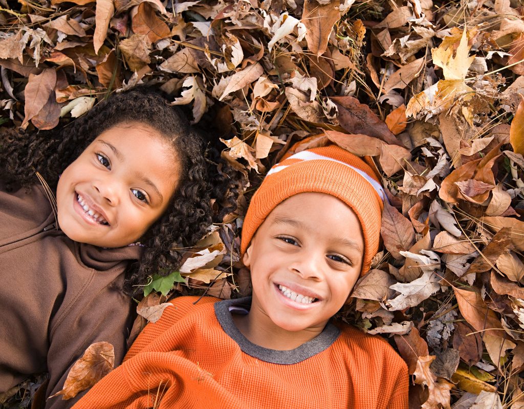 A couple of kids lying in a pile of leaves