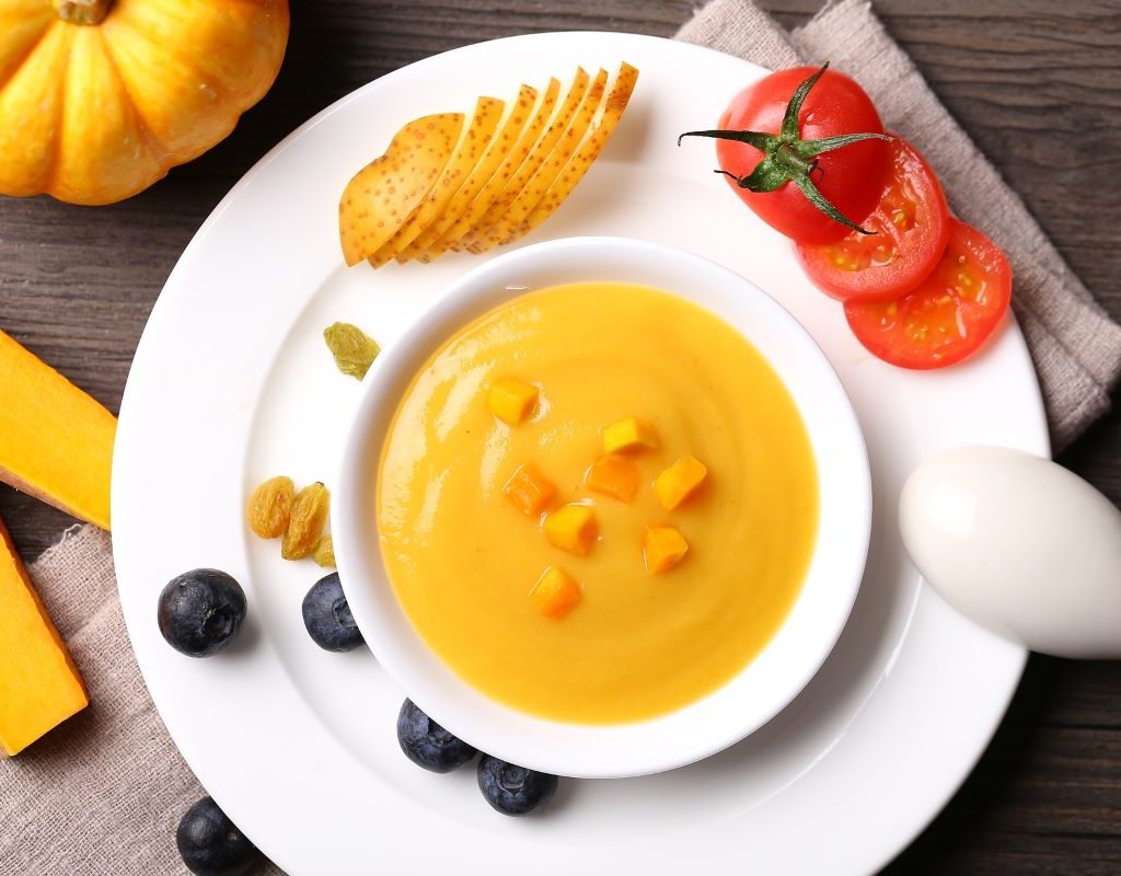 Squash soup surrounded by tomato and blueberries on a plate