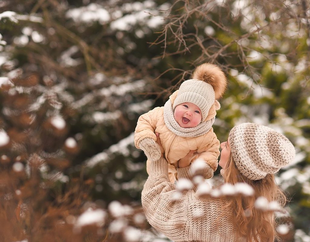 A parent holding up a baby outside in the snow