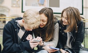 protecting tweens online smiling friends using mobile phone while sitting at bus stop