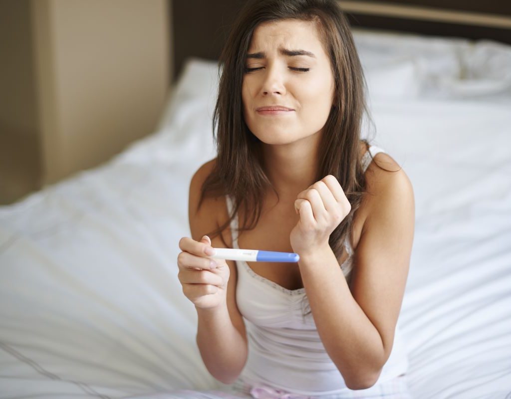 lady sitting on bed holding a pregnancy test