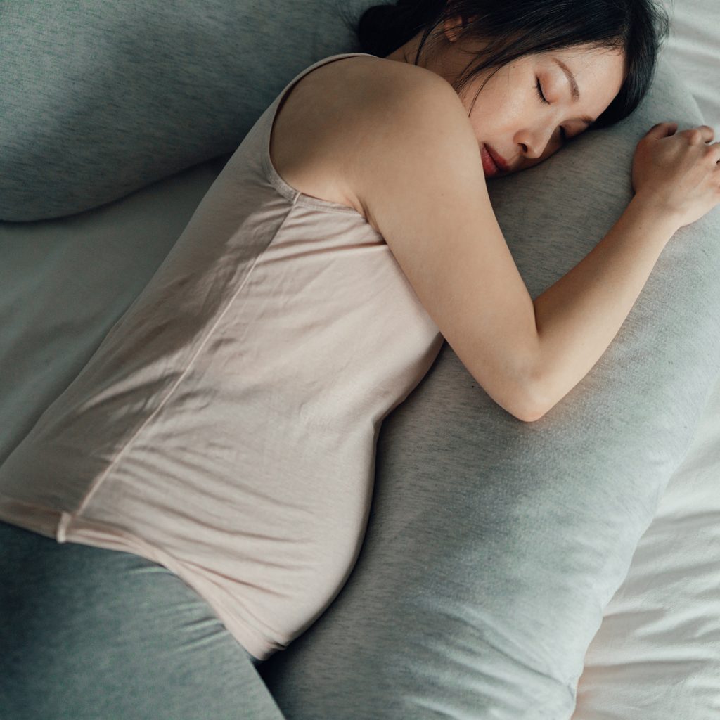 Pregnant Woman Sleeping In Bed With Maternity Pillow