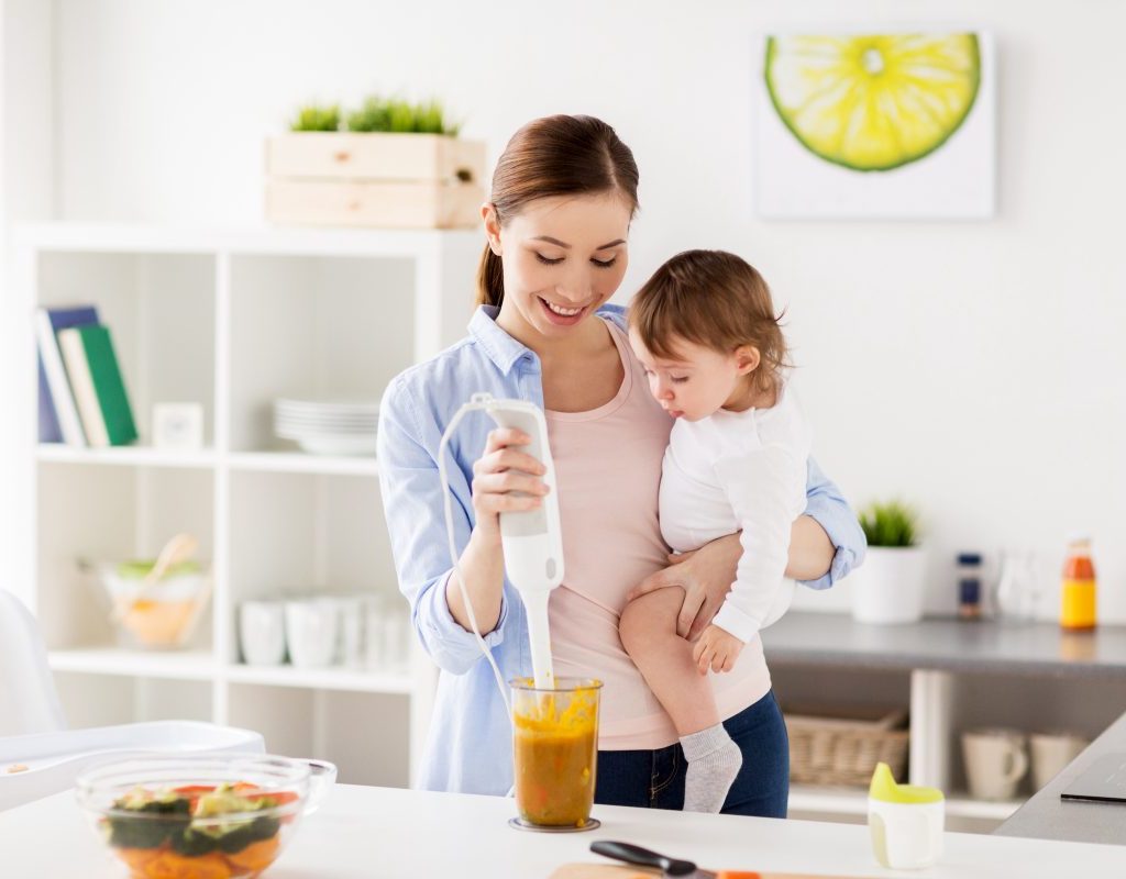 A mother holding her baby while making baby food.