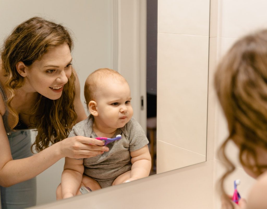 A mom holds the toothbrush for the baby