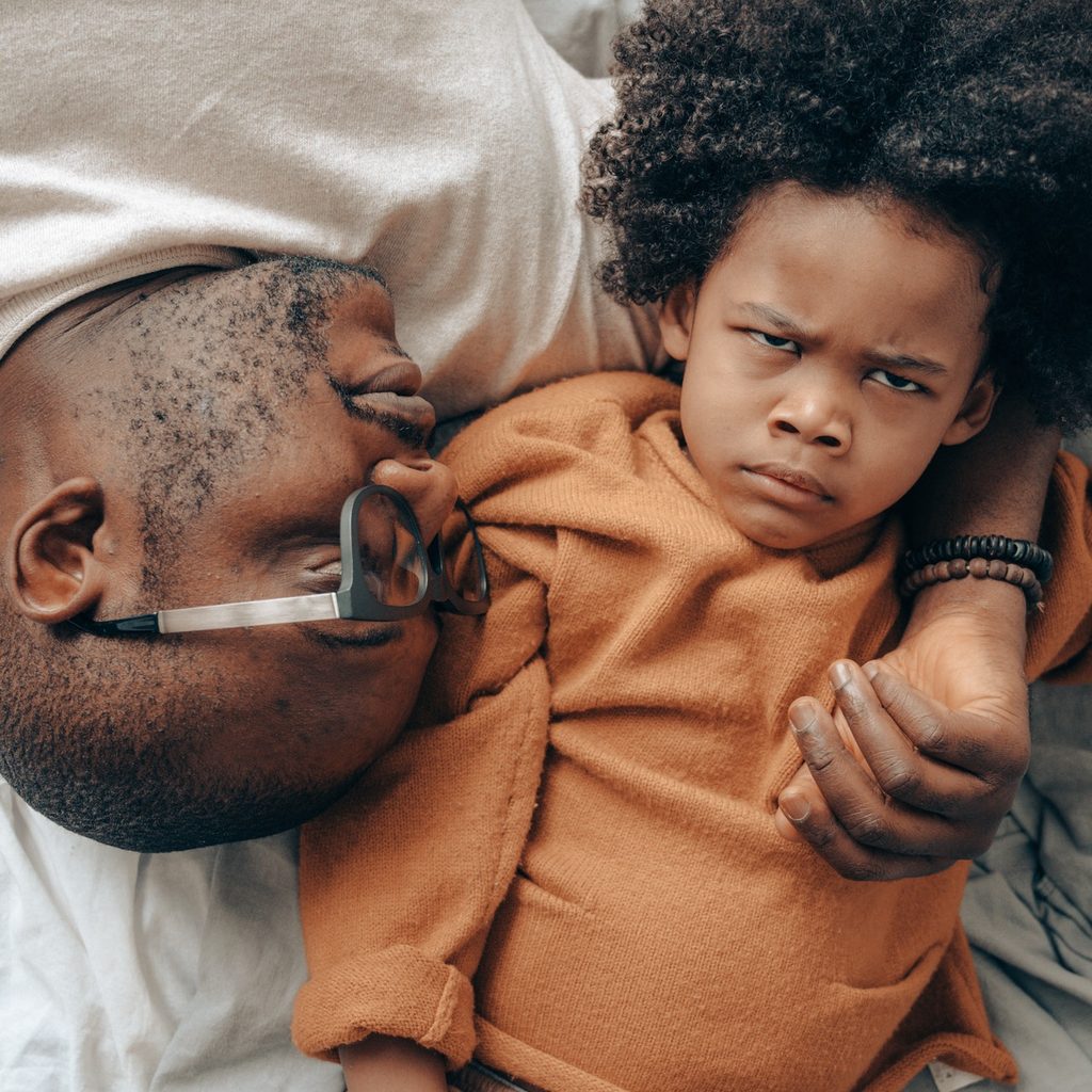 Angry child lying on bed with father
