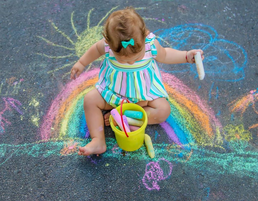 Baby girl sitting on chalk drawing of a rainbow