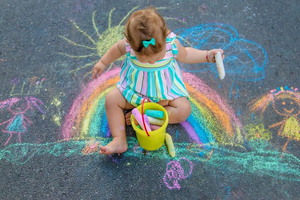 Baby girls with chalk sitting in the middle of a chalk rainbow