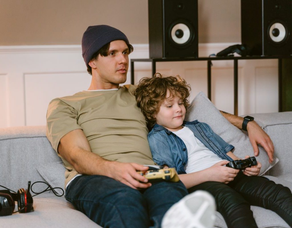 Father and son sitting on couch holding game controllers