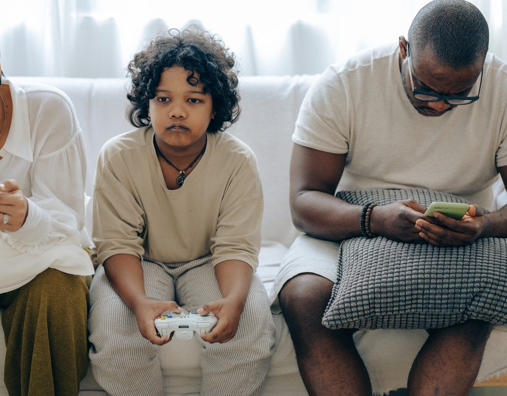 Child playing video game sitting in between parents on phones