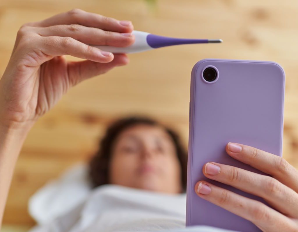 Lady looking at thermometer and cell phone