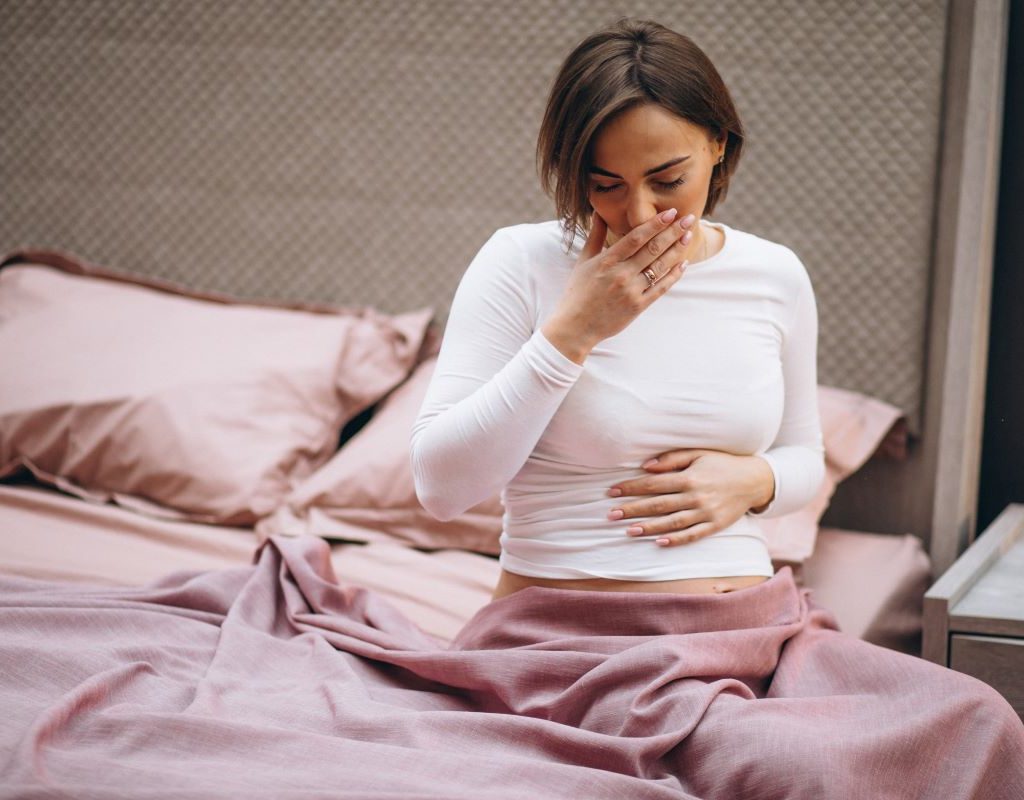 Lady sitting at edge of bed with her hand on her mouth