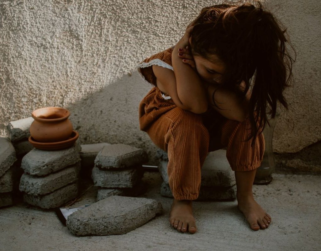 Little girl with head down sitting on sidewalk