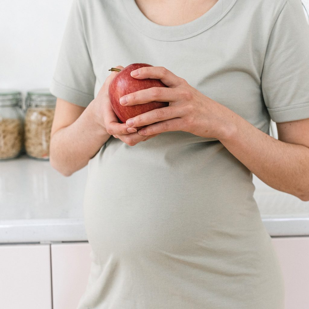 Pregnant person holding an apple.