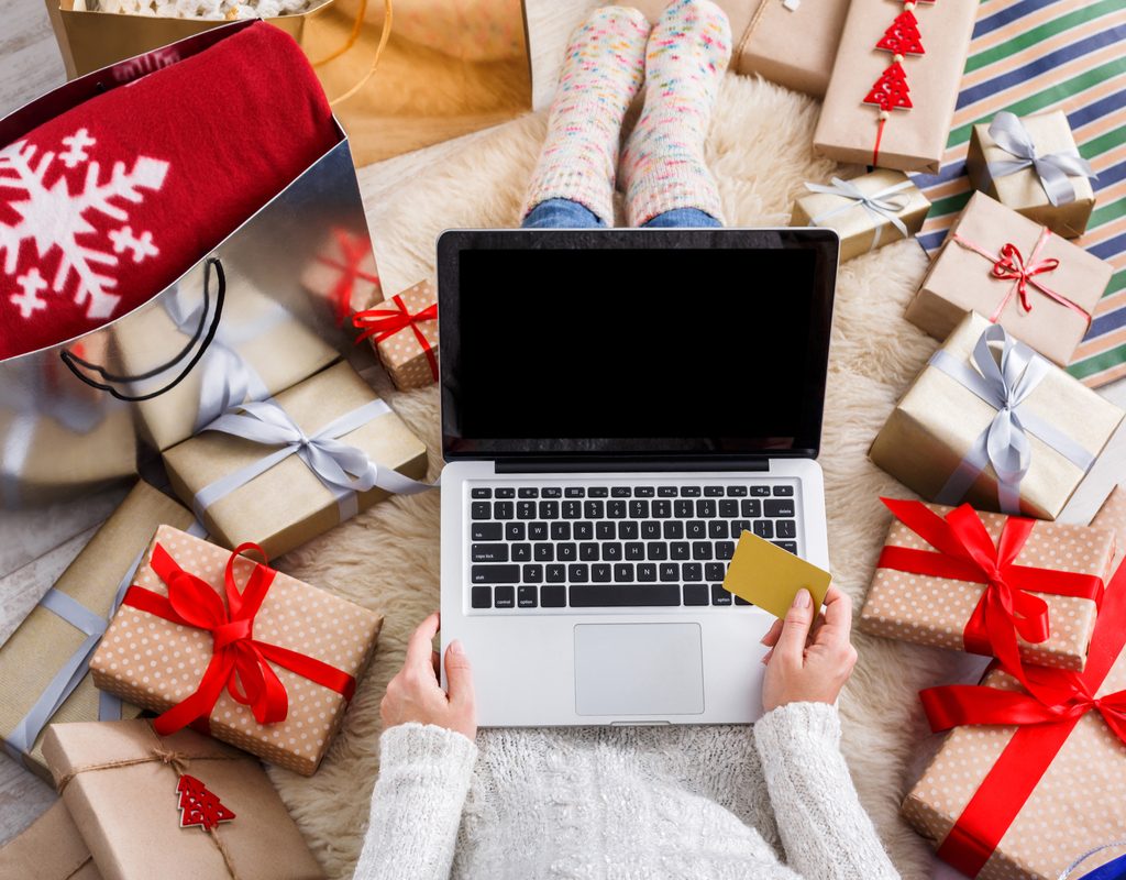 A person doing holiday shopping on their laptop with presents all around them