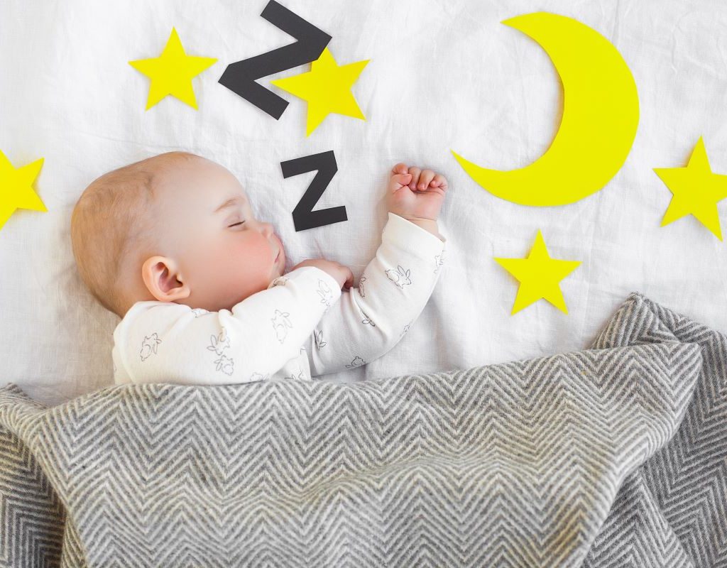 Baby sleeping in crib with a gray blanket and decals