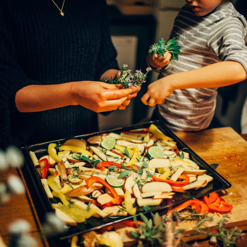 Young boy sprinkling fresh herbs on vegetable dish