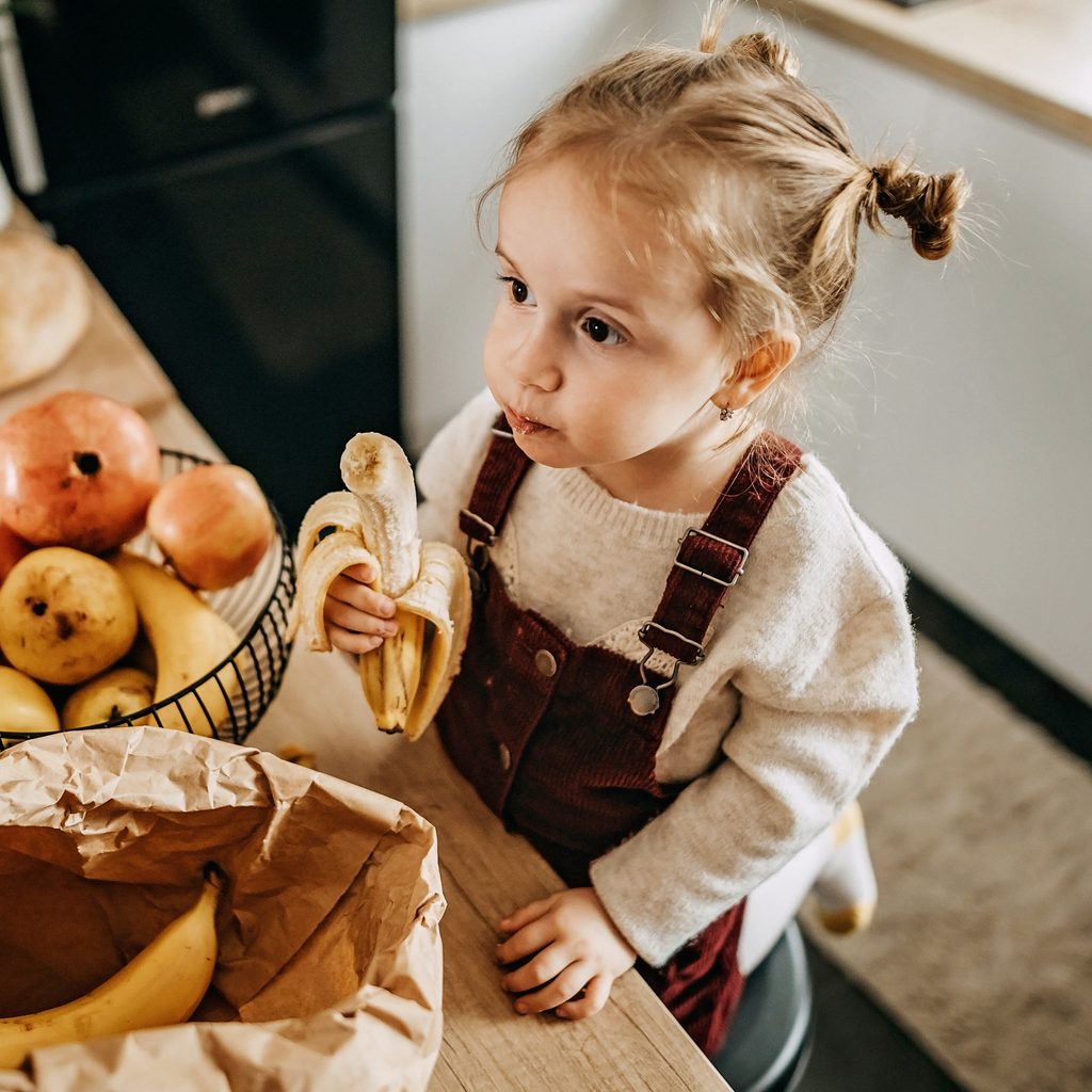 Toddler girl eating fruit in the kitchen