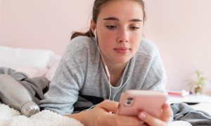 A teenager lies on her bed looking at her phone