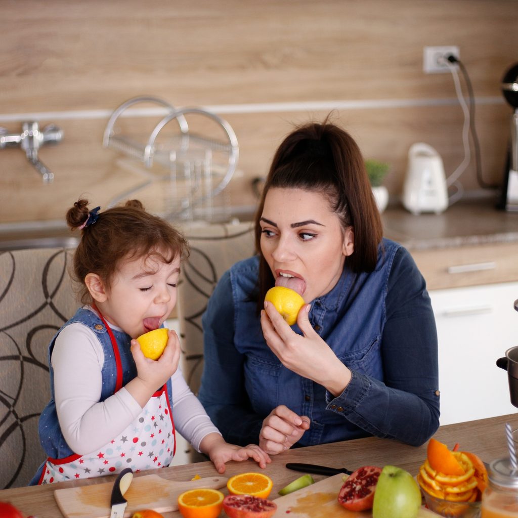 Mother and daughter making faces after licking raw lemons together