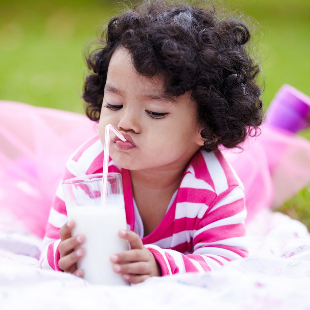 Toddler girl drinking milk through a straw while lying on the grass