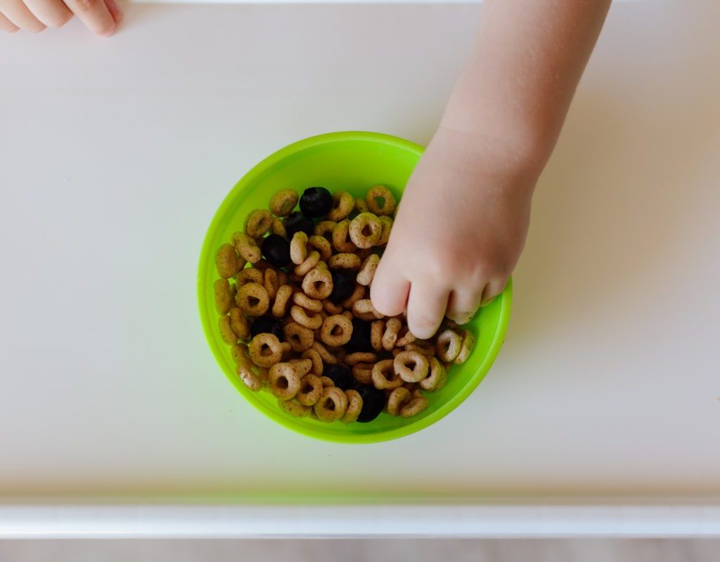 A small child grabbing cereal from a bowl