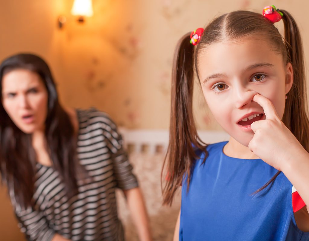 A young girl picking her nose with her mother in the background looking grossed out.