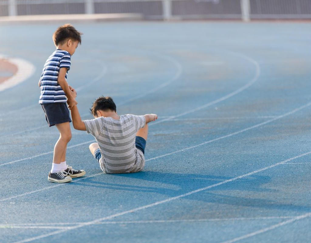 One boy helping another boy to stand up