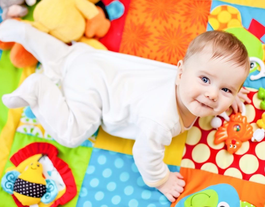 A baby looking up over their shoulder while on a play mat