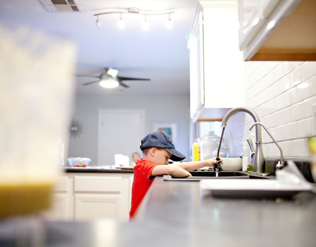 A boy is rinsing dishes with the sprayer on the kitchen faucet