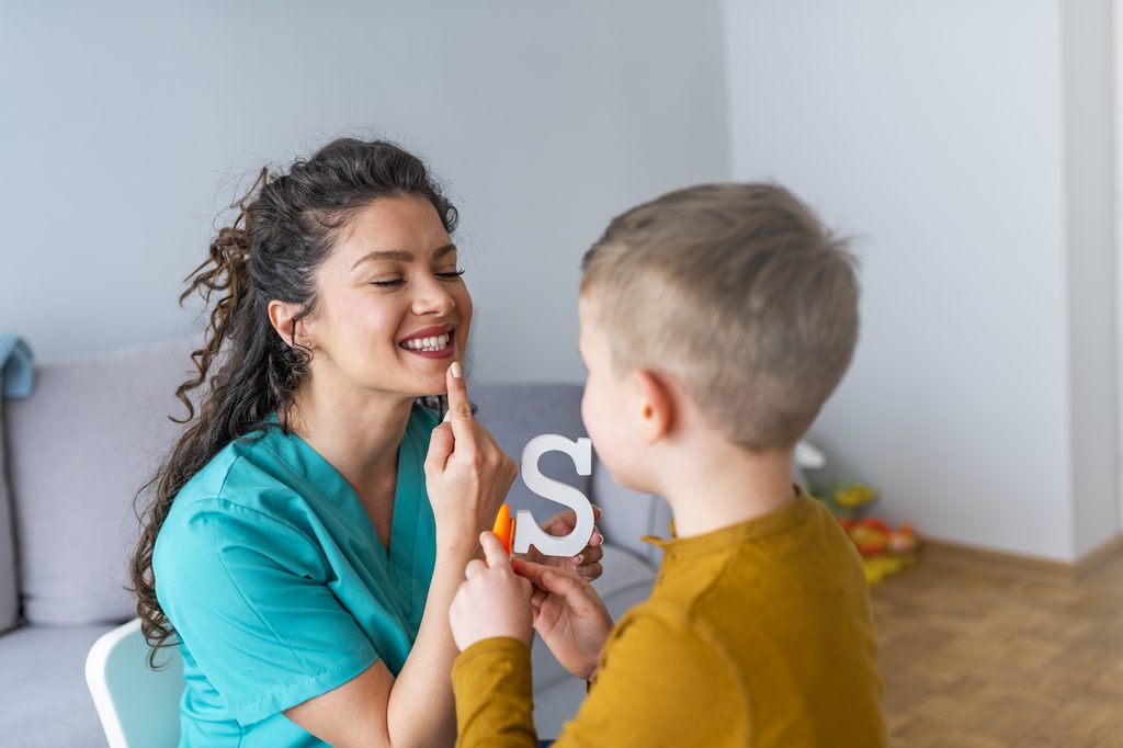 Stuttering boy and speech therapist doing exercises. Boy and young woman teacher during private home lesson. Shot of a speech therapist and a little boy