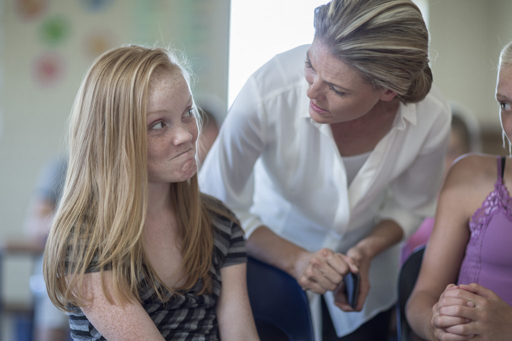 Teacher with cell phone in classroom scolding schoolgirl