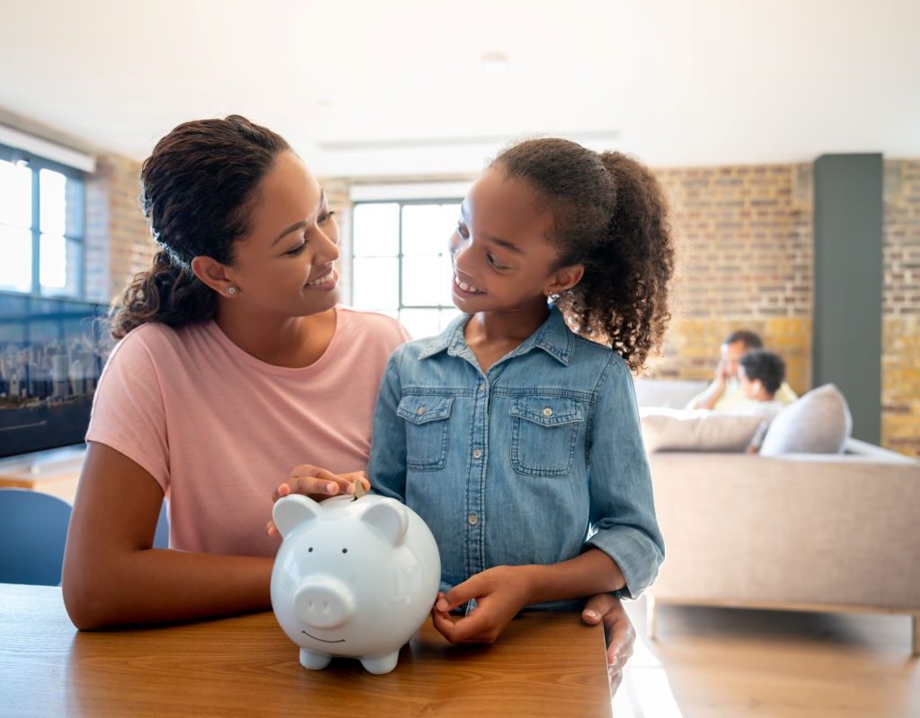 Daughter placing money in piggy bank as Mom watches