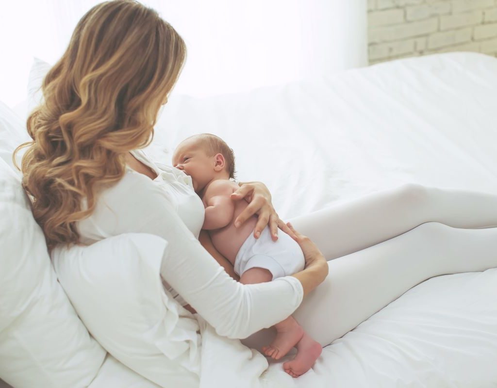 Mom breastfeeding newborn in bed.