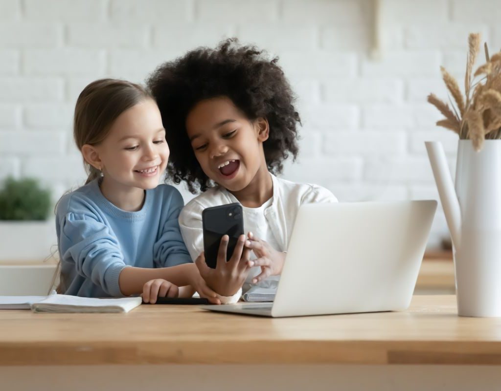 Two girls sharing a cell phone in front of a laptop