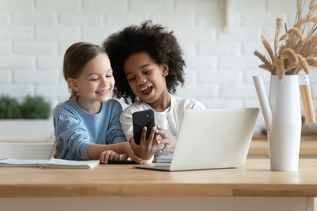 Two girls sharing a cellphone in front of a laptop
