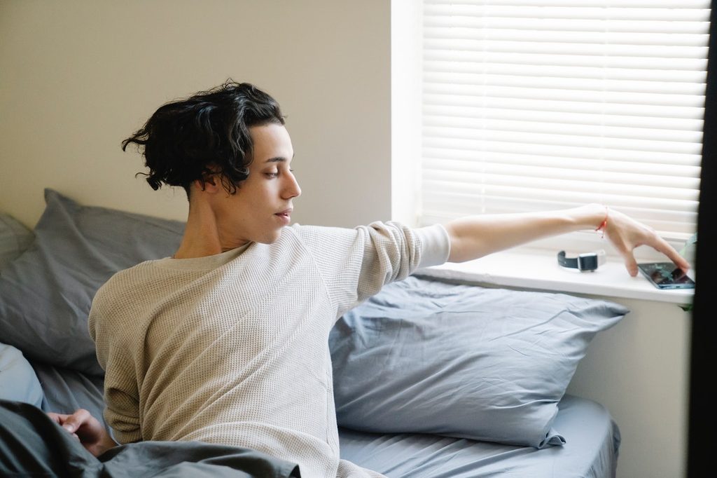 Boy sitting in bed reaching for smartphone