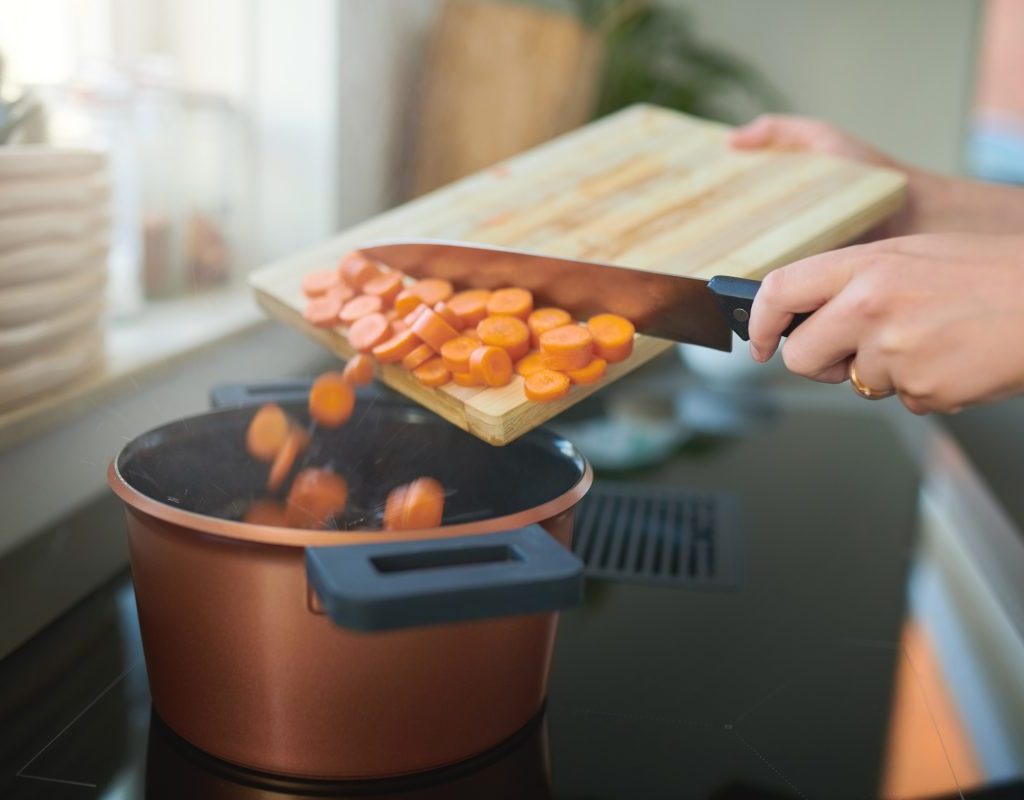 Person adding carrots to a pot on the stove