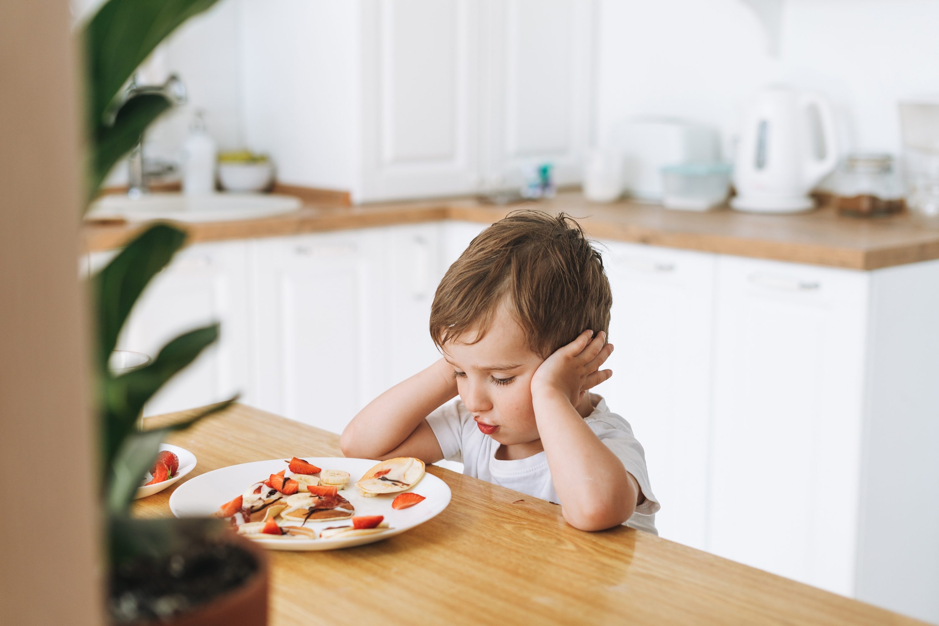 A toddler sitting down with a plate of food.