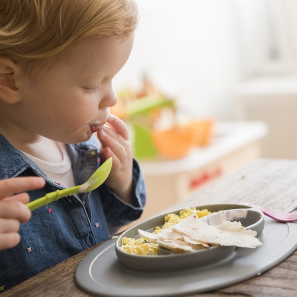 Toddler girl eating with fingers and spoon