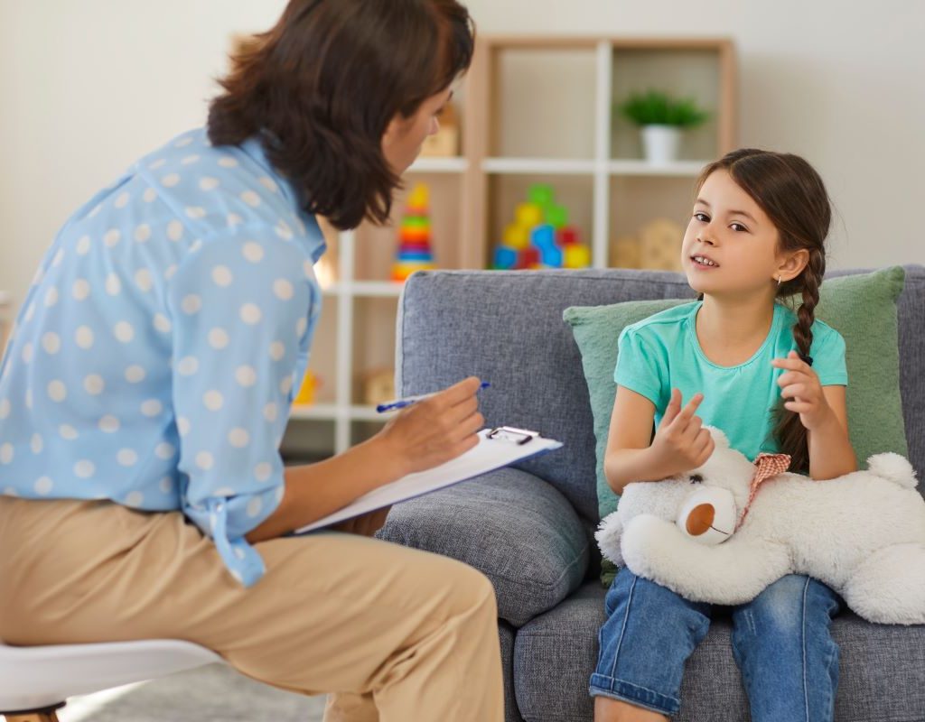 Girl sitting and holding a stuffed animal while talking to therapist