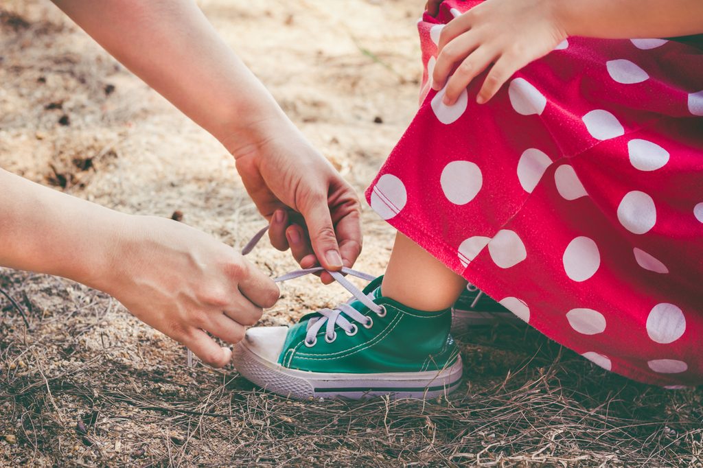A parent teaching a toddler girls how to tie her sneaker